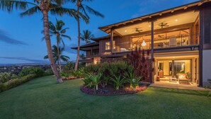 A two-story house with a balcony, surrounded by a well-maintained lawn and palm trees.