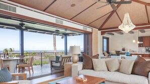 A spacious living area with a large sofa, a coffee table, and a balcony with a view of the ocean.