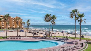 Un complexe hôtelier doté d’une piscine, d’une plage, de palmiers et offrant une vue sur l’océan.