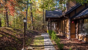 A pathway leading to a building with a covered porch, surrounded by trees and a forested area. - American themed 9BR (sleeps 43) cabin in GBurg with tons of games and space! (GATLINBURG)