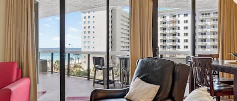 A hotel room with a balcony, a red sofa, a leather chair, and a dining table.
