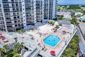 A high-rise hotel with a rooftop pool, multiple balconies, and a landscaped area with sun loungers and umbrellas.