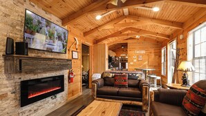 Ein gemütliches Blockhaus-Interieur mit Kamin, Holzwänden, Fernseher und einer Couch.
