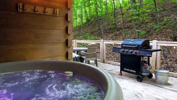 Ein Whirlpool auf einer Holzterrasse mit Grill und Stühlen.