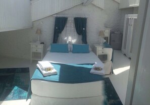 Une chambre d’hôtel comprenant un lit, deux tables de chevet, une commode, une fenêtre avec des rideaux et un système de climatisation intégré.