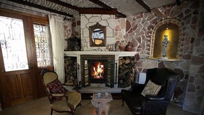 A cozy living room with a stone fireplace, two armchairs, a small table, and a decorative mirror above the fireplace. - Mel'Dem Butik Otel (Cesme)