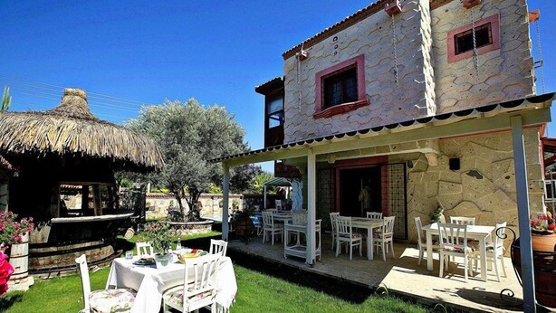 A two-story stone house with a covered patio area, outdoor seating, and a thatched-roof structure. - Mel'Dem Butik Otel (Cesme)