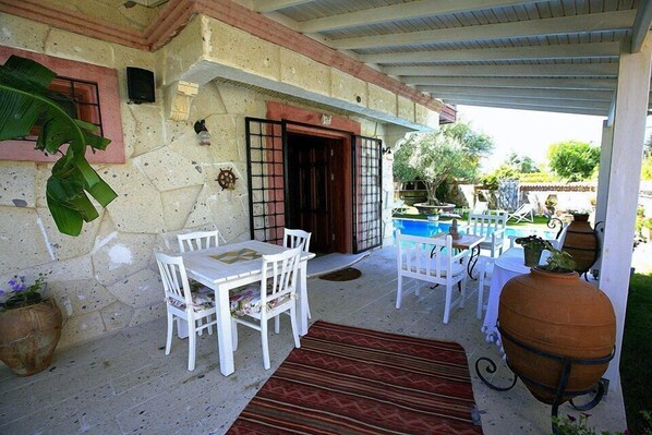 Un patio cubierto con mobiliario blanco, una pared de piedra y una zona de piscina.