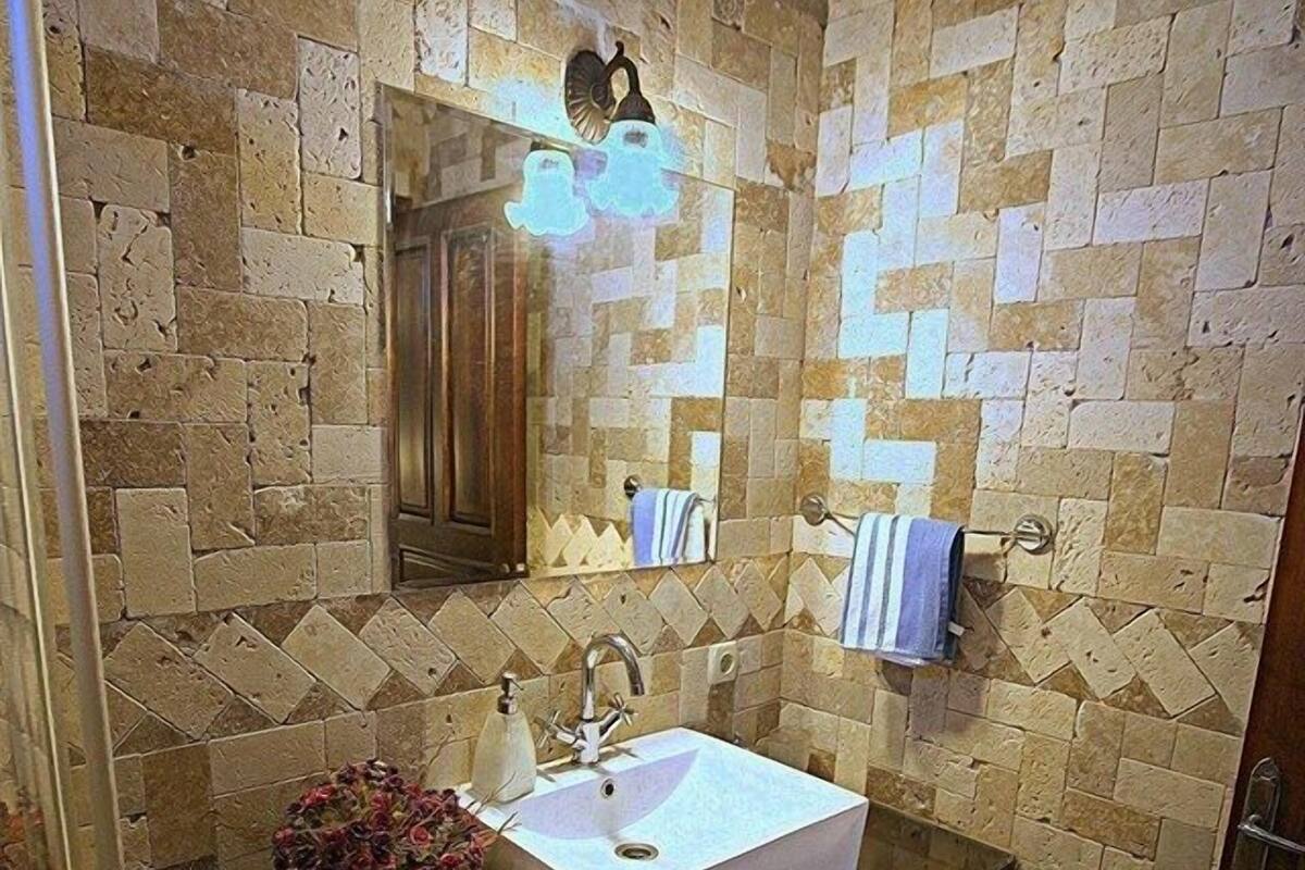 A bathroom with a stone mosaic wall, a white sink, a wooden vanity, and a mirror.