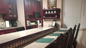 Un comedor con una mesa larga, sillas, una cocina al fondo y una ventana con persianas.