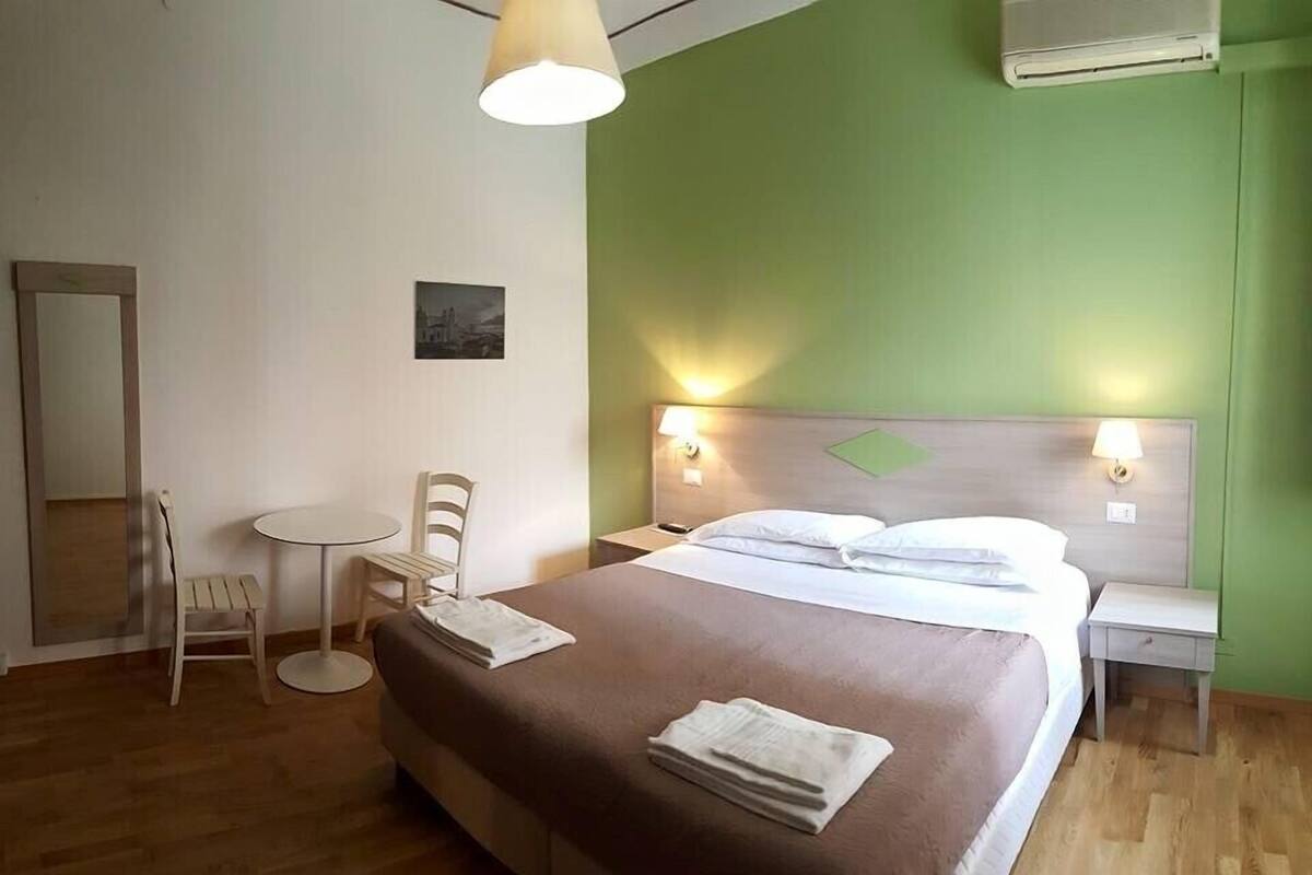 Ein Hotelzimmer mit Bett, Nachttischen, einem Sessel, einem kleinen Tisch und einer Klimaanlage.