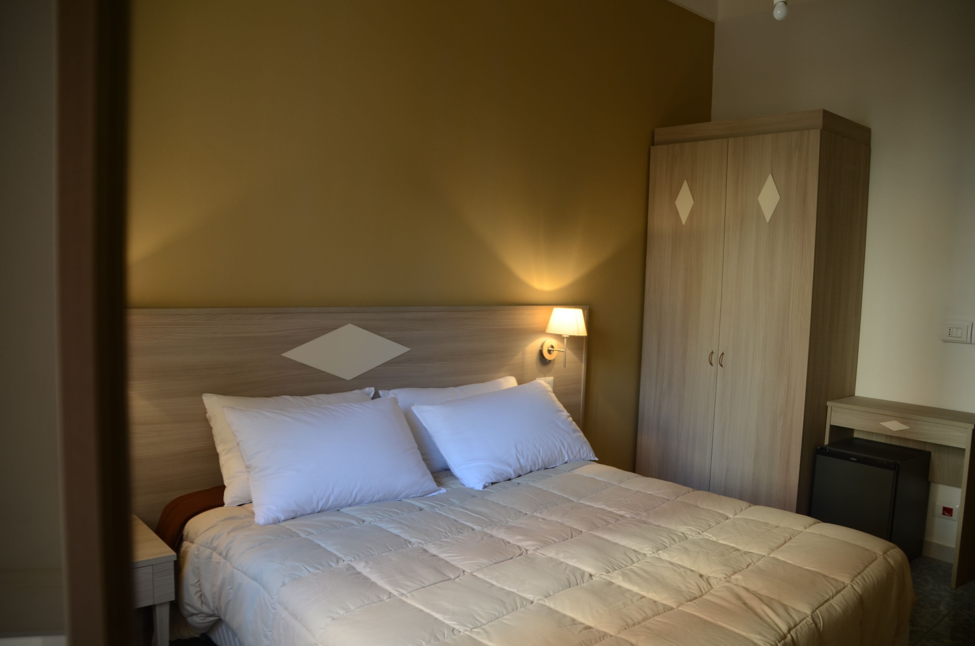Un lit bien fait, avec une tête de lit, une lampe de chevet et une armoire.
