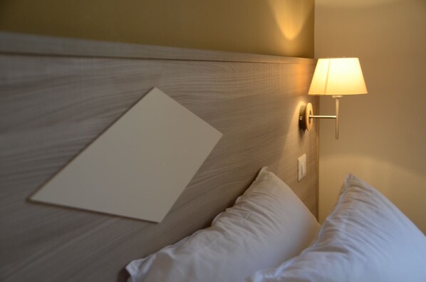 Une chambre d’hôtel avec une tête de lit en bois, une lampe de chevet et deux oreillers.