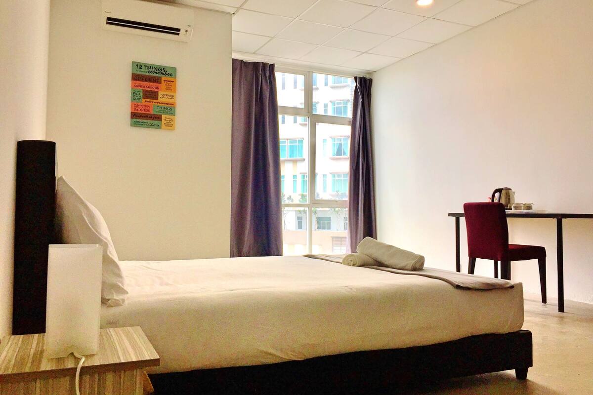 Una habitación de hotel con cama, escritorio, silla y ventana con cortinas.