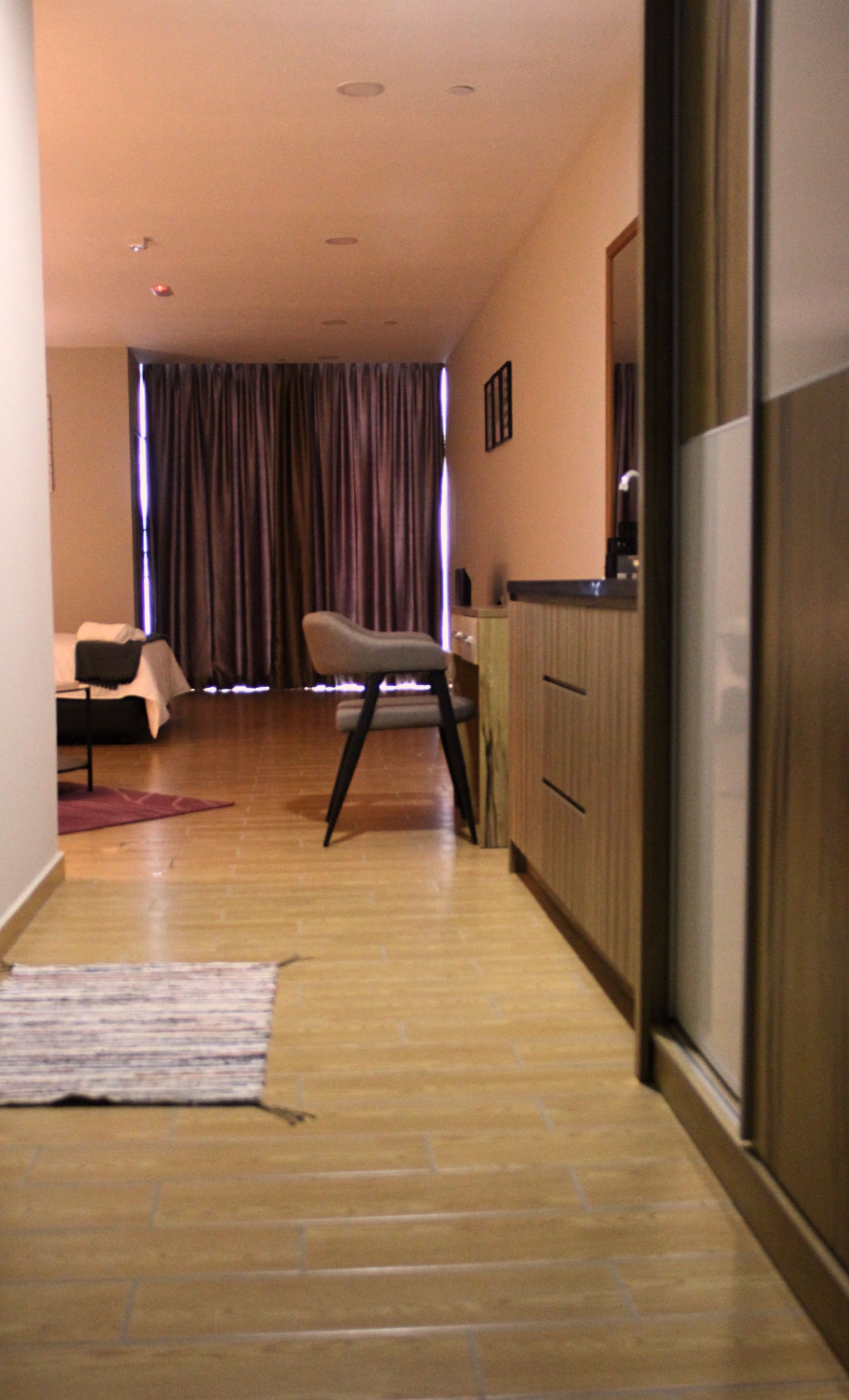 Un pasillo estrecho con suelo de madera, una silla, una cama y una mesita.