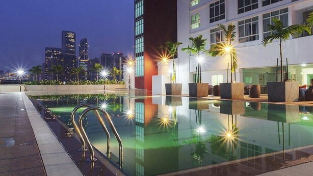 Piscina moderna de hotel con vista al horizonte de la ciudad, palmeras y un área junto a la piscina bien iluminada.