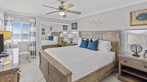 Een slaapkamer met een groot bed, nachtkastjes, een bureau en een plafondventilator.