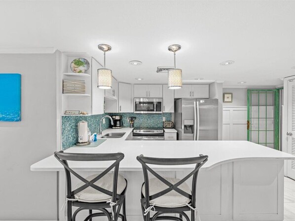 A modern kitchen with white cabinetry, a central island with two barstools, and pendant lighting. - 302- Beautiful Gulf-Front condominium With Exceptional Views! (Destin)
