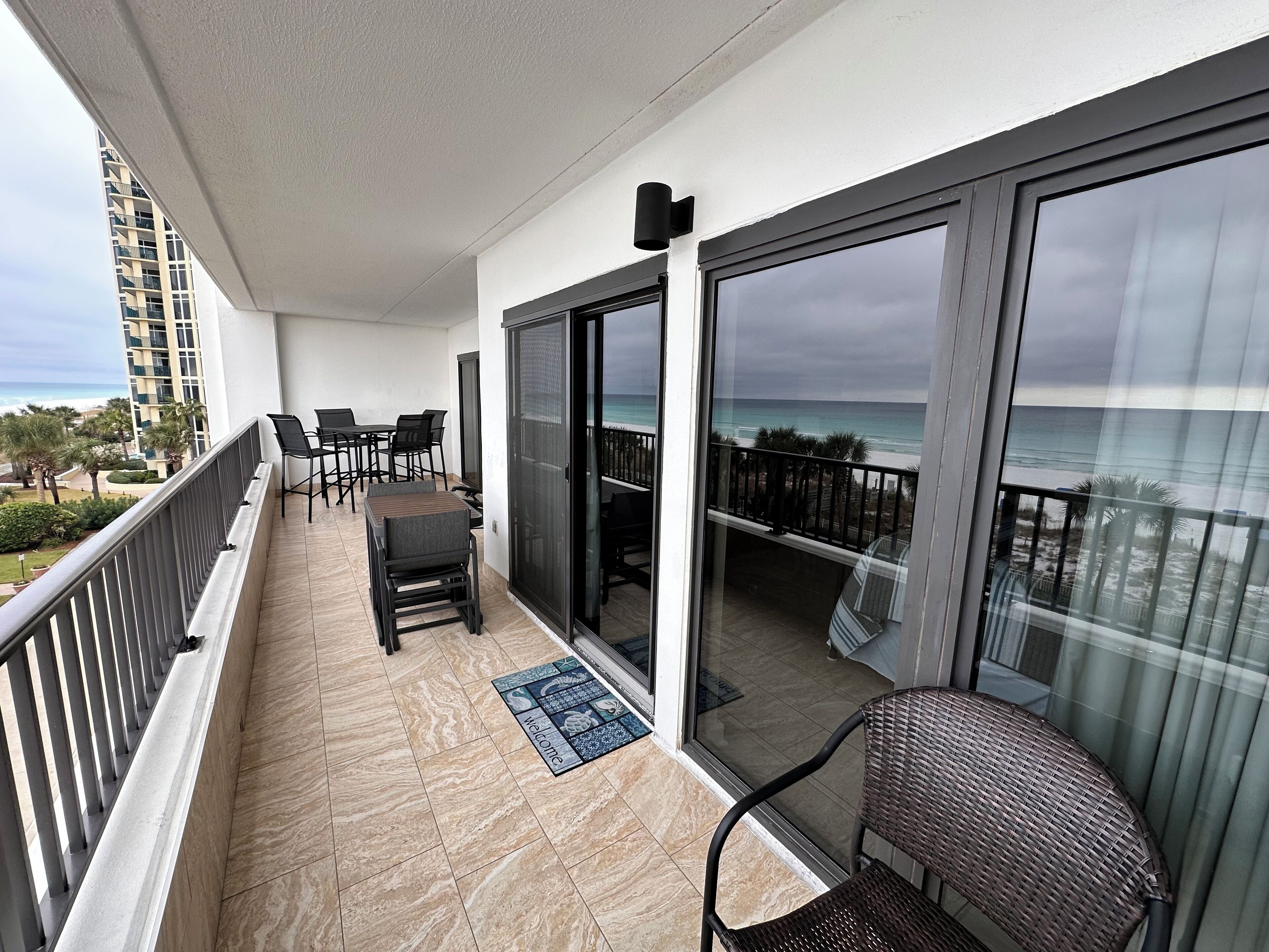 Un balcone con vista sull'oceano, arredato con sedie e un tavolo, e un tappetino di benvenuto.