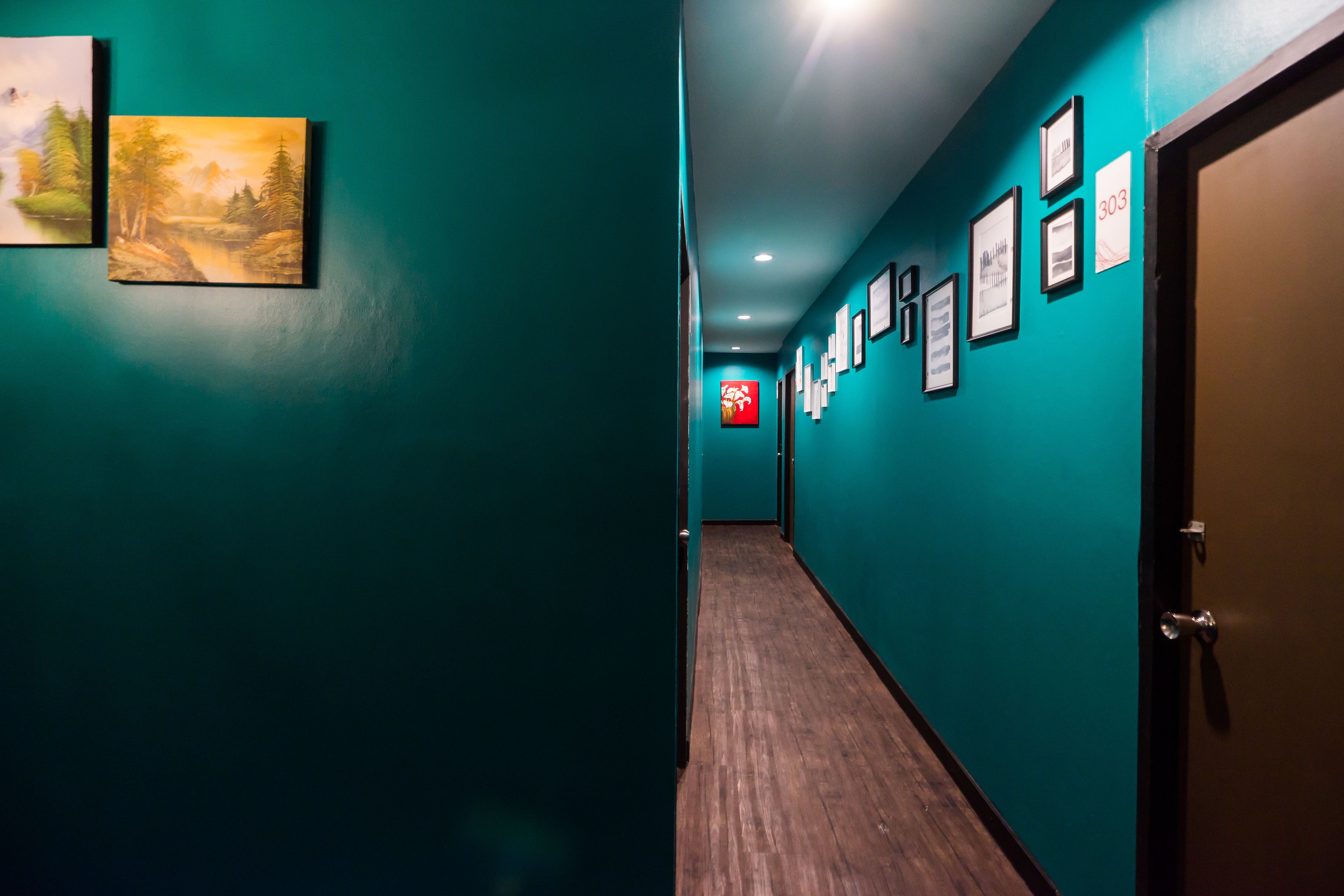 Un couloir aux murs de couleur turquoise, doté d’un plancher en bois et orné de tableaux encadrés.