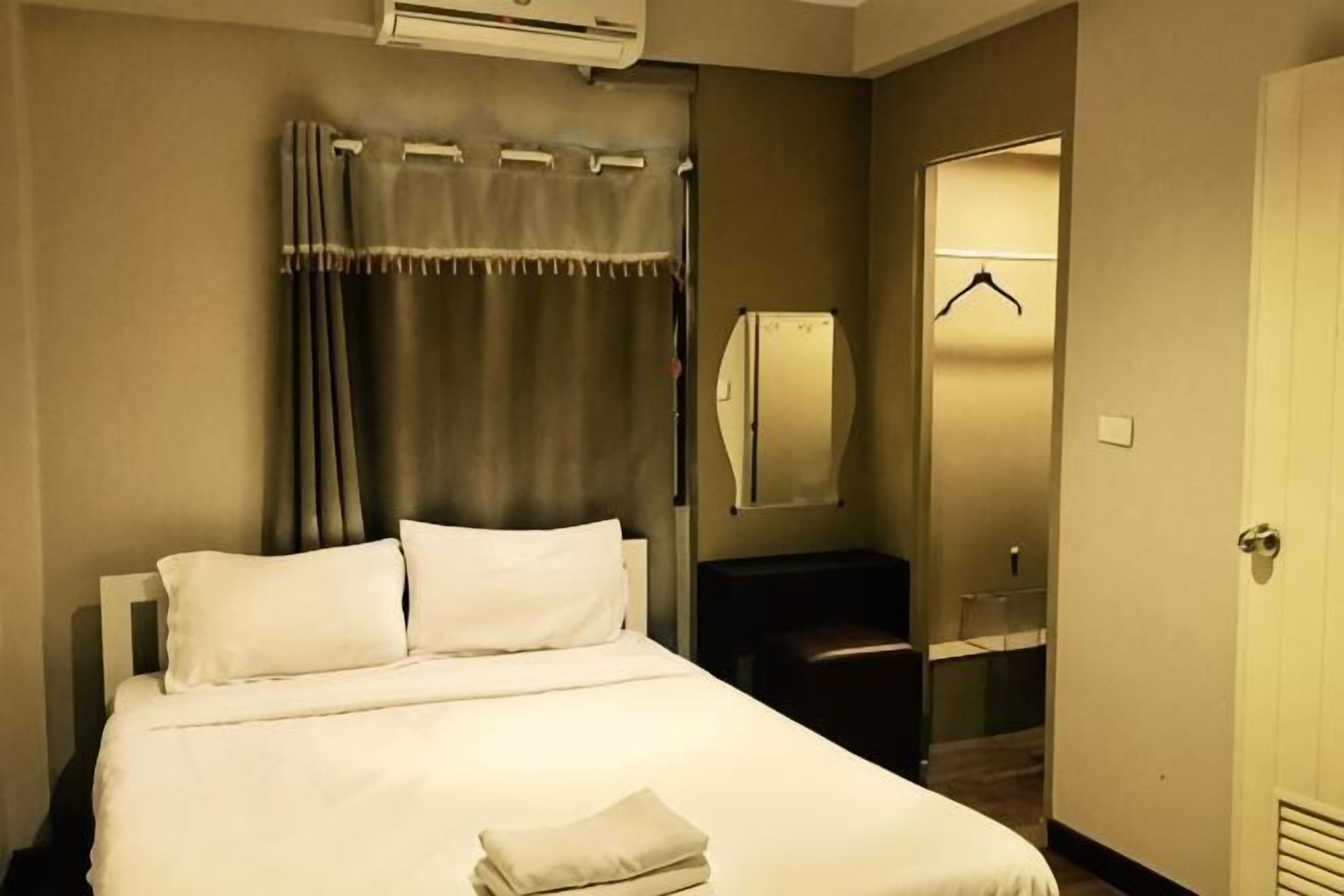 A hotel room with a bed, a mirror, a coat rack, and a door.