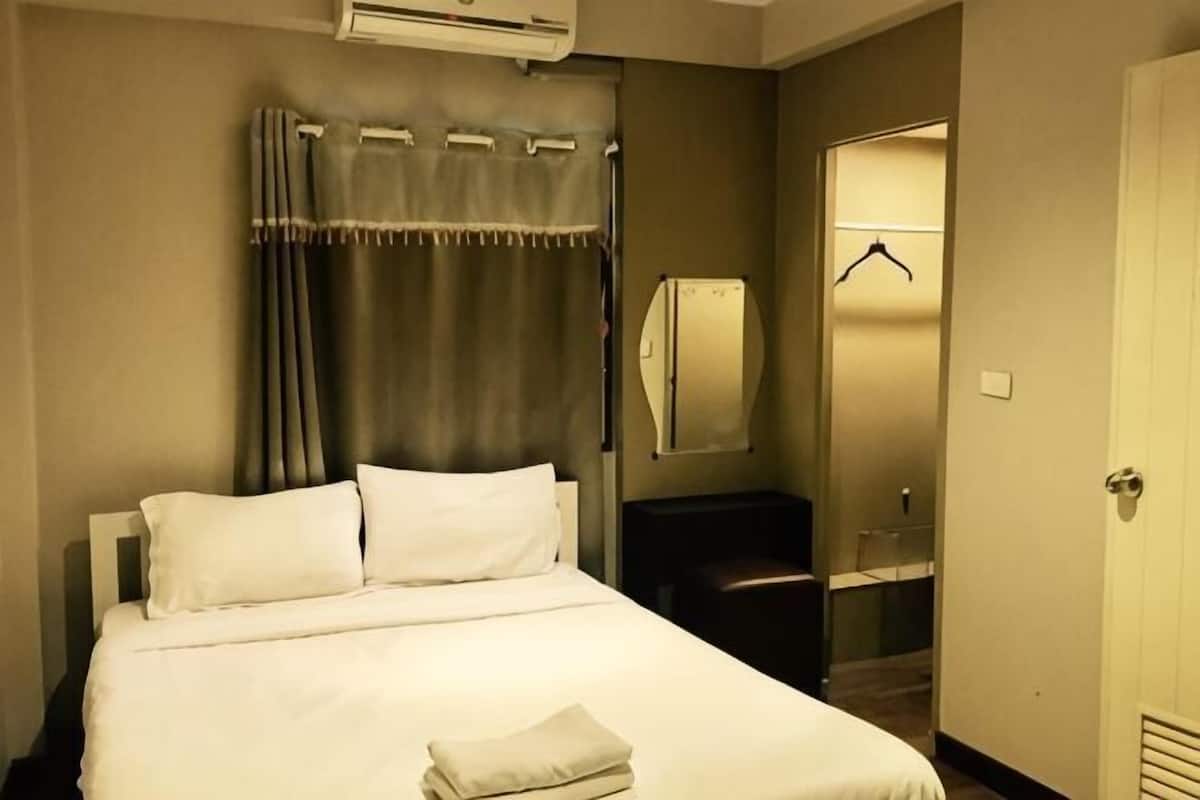 A hotel room with a bed, a mirror, a coat rack, and a door.