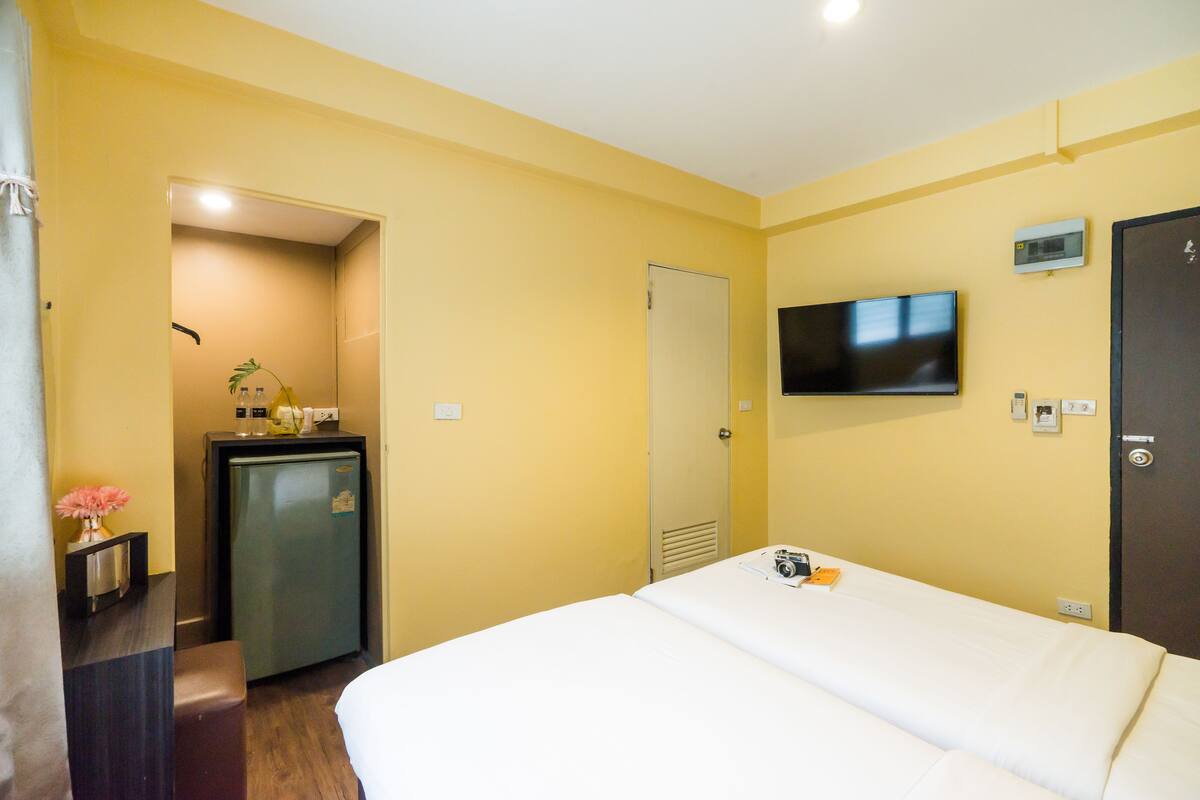 A hotel room with a bed, a TV mounted on the wall, a small refrigerator, and a door leading to another room.