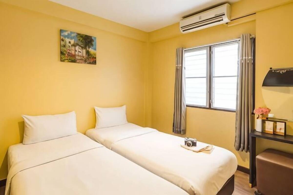 A hotel room with two beds, a window with curtains, an air conditioning unit, and a painting on the wall.