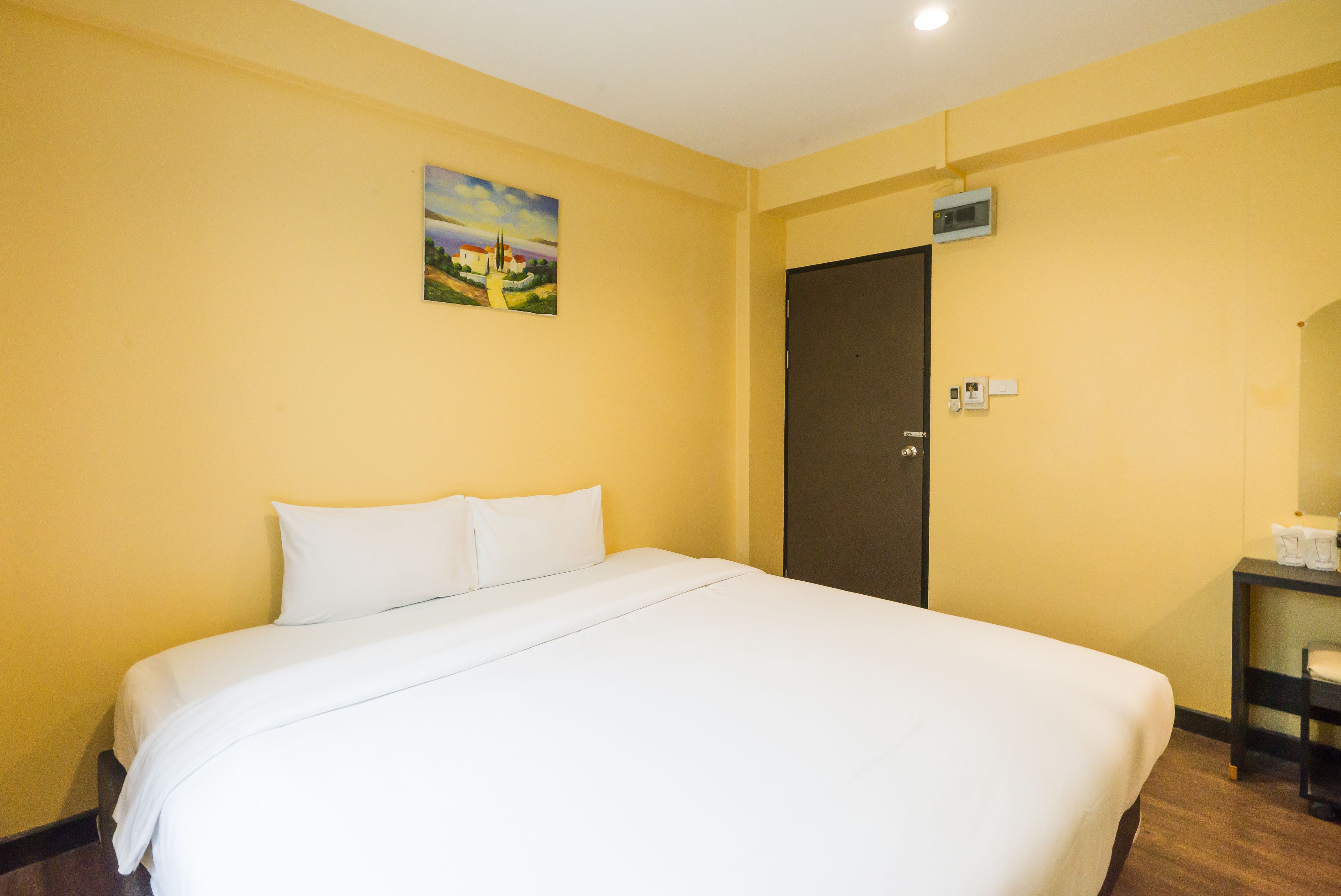 A hotel room with a large bed, a painting on the wall, a door, and a small table with a chair.