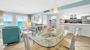 Een moderne woonkamer met een glazen eettafel, een teal fauteuil en uitzicht op de oceaan.