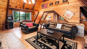 A log cabin interior with a wooden ceiling, a large window, a fireplace, a sofa, and a coffee table. - A-Frame cabin- 3BR, pet friendly, hot tub, located between GBurg & Pigeon Forge! (Sevierville)