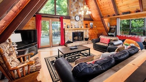 A cozy log cabin interior with a stone fireplace, leather sofas, and a television. - A-Frame cabin- 3BR, pet friendly, hot tub, located between GBurg & Pigeon Forge! (Sevierville)
