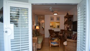 An open door leading to a living room with wicker furniture, a ceiling fan, and a dining area. - Truman Annex Gem Shipyard 2BR C  Walk to Beach & Bars, Best of Old Town (Key West)