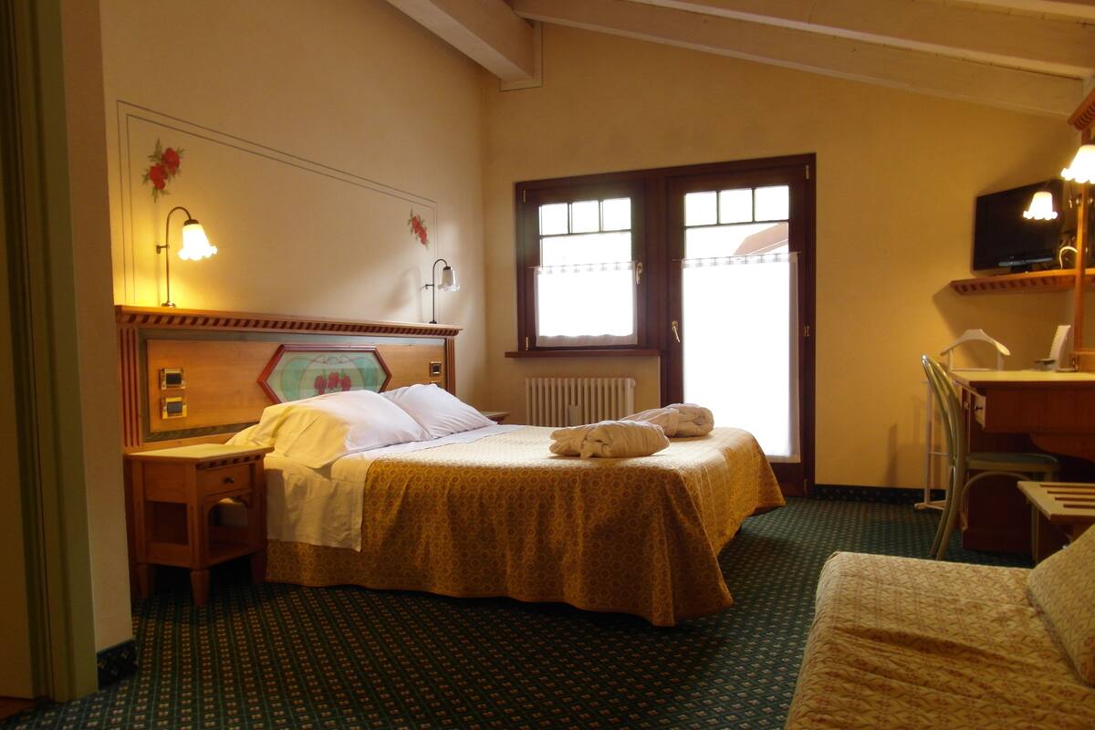 A hotel room with a bed, a desk, a chair, a radiator, and a television.