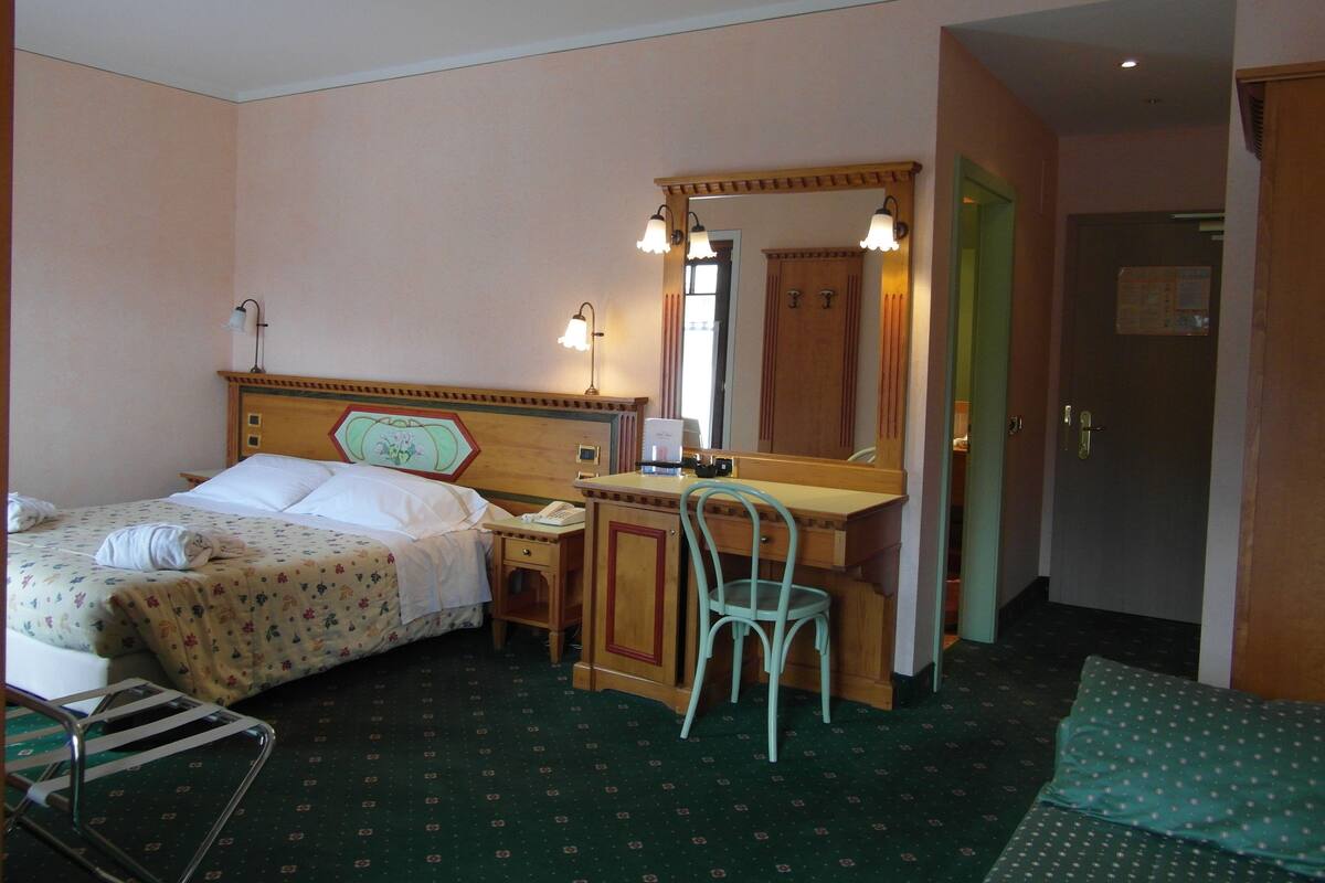 A hotel room with a bed, a desk, a chair, and a mirror.