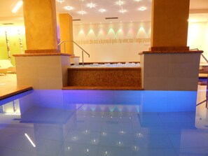 A modern indoor pool area with a marble floor, a central staircase, and a wall with a quote. - Ideal (Pinzolo)