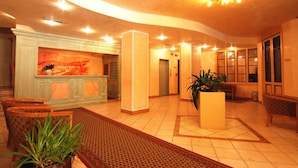 A hotel lobby with a reception desk, seating area, and a large plant. - Ideal (Pinzolo)