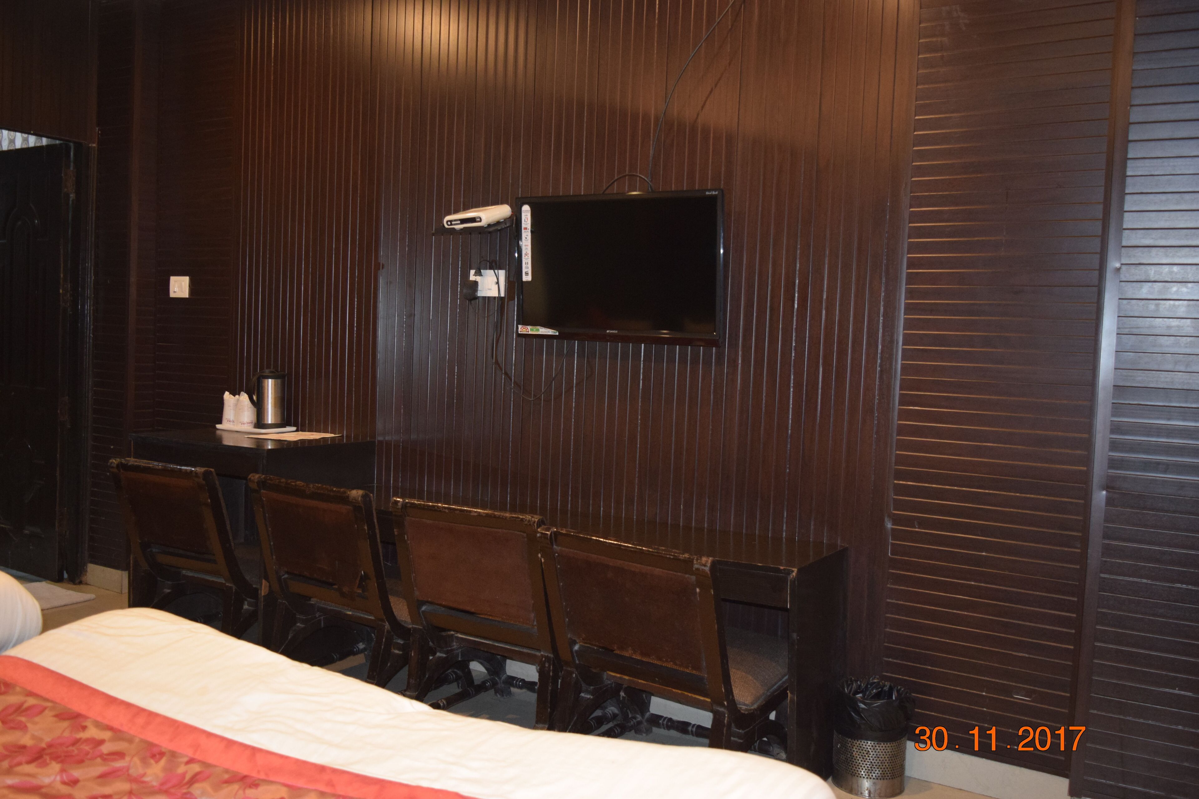 Habitación de hotel con una cama grande, un televisor montado en la pared y cuatro sillas de madera.
