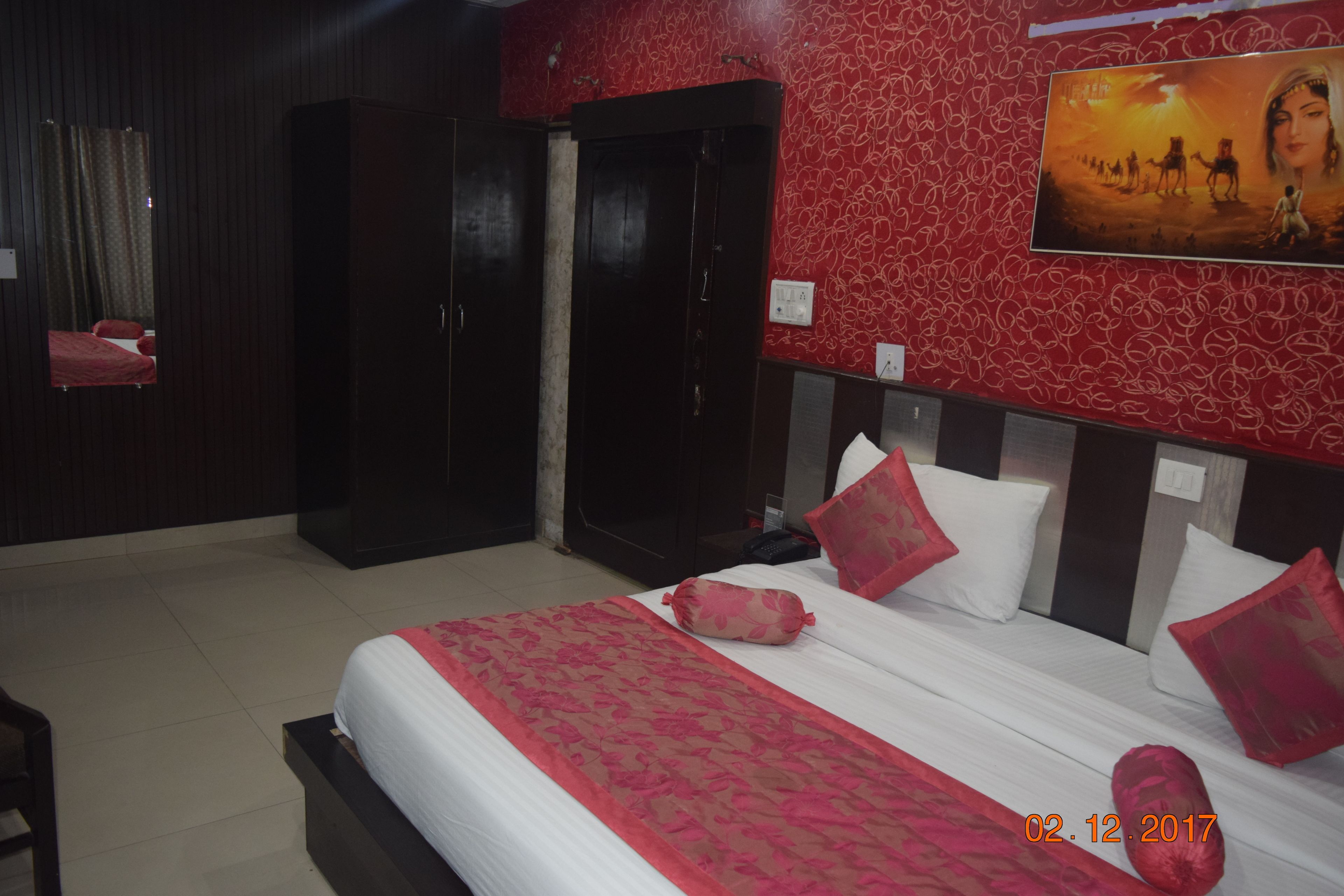 A hotel room with a large bed, red and white patterned walls, a painting, and a wardrobe.