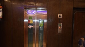 Interior de elevador com parede de madeira, dois painéis de vidro e um visor digital.