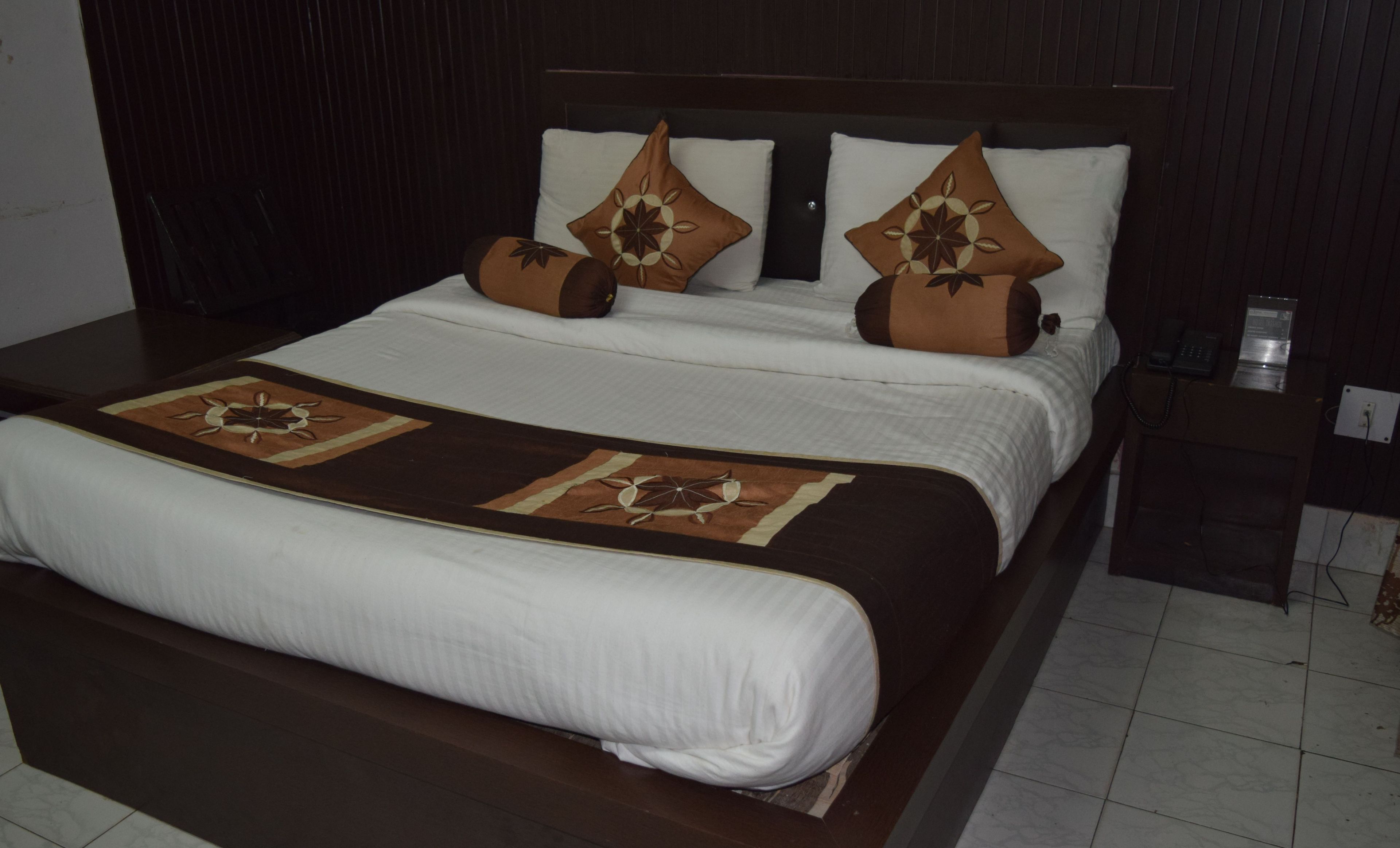 A neatly made bed with a brown headboard, white bedding, and decorative pillows.