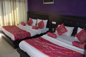 A hotel room with two beds, each with white linens and red decorative pillows.