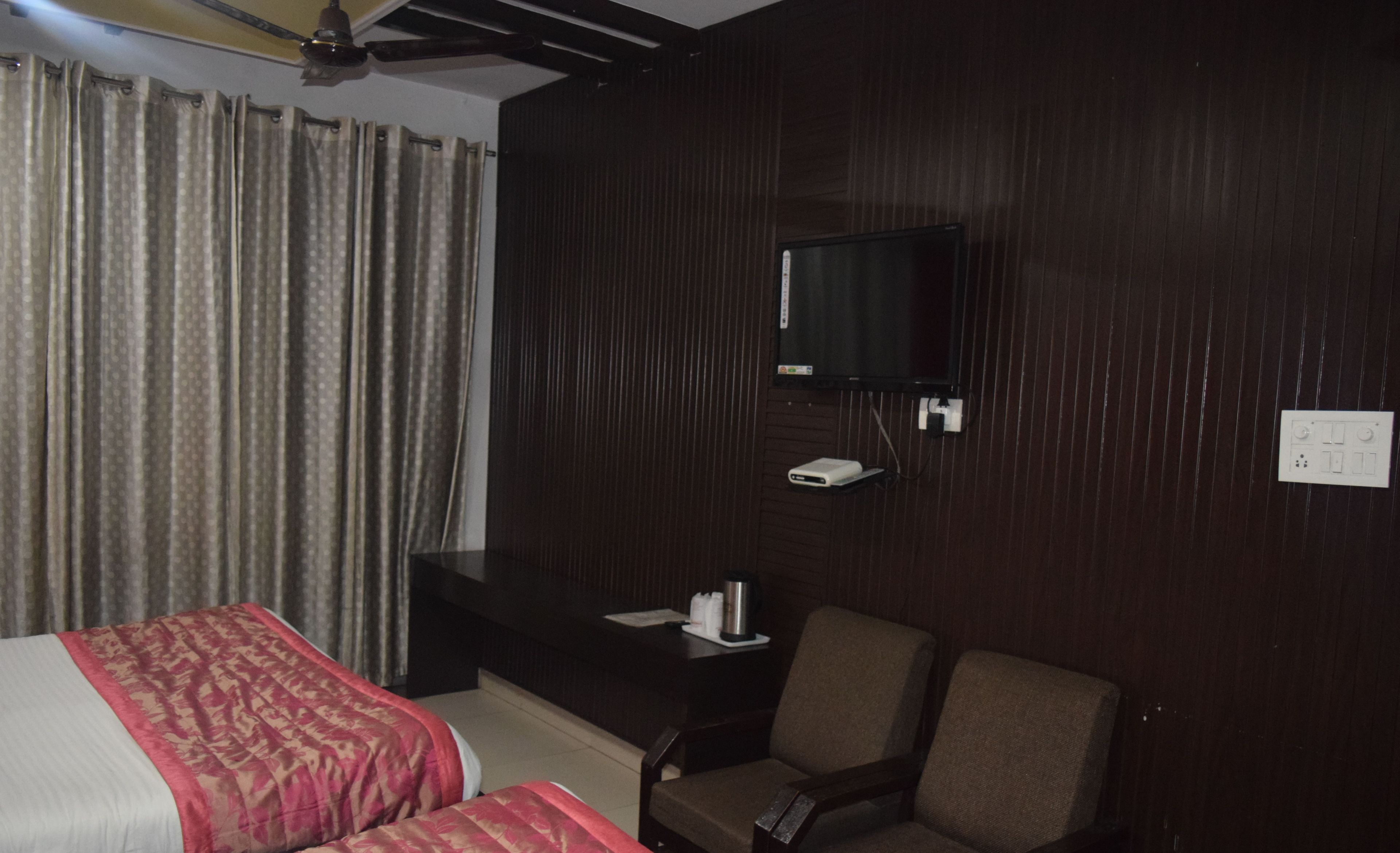 Una habitación de hotel con cama, una silla, escritorio, televisión y toma de corriente.