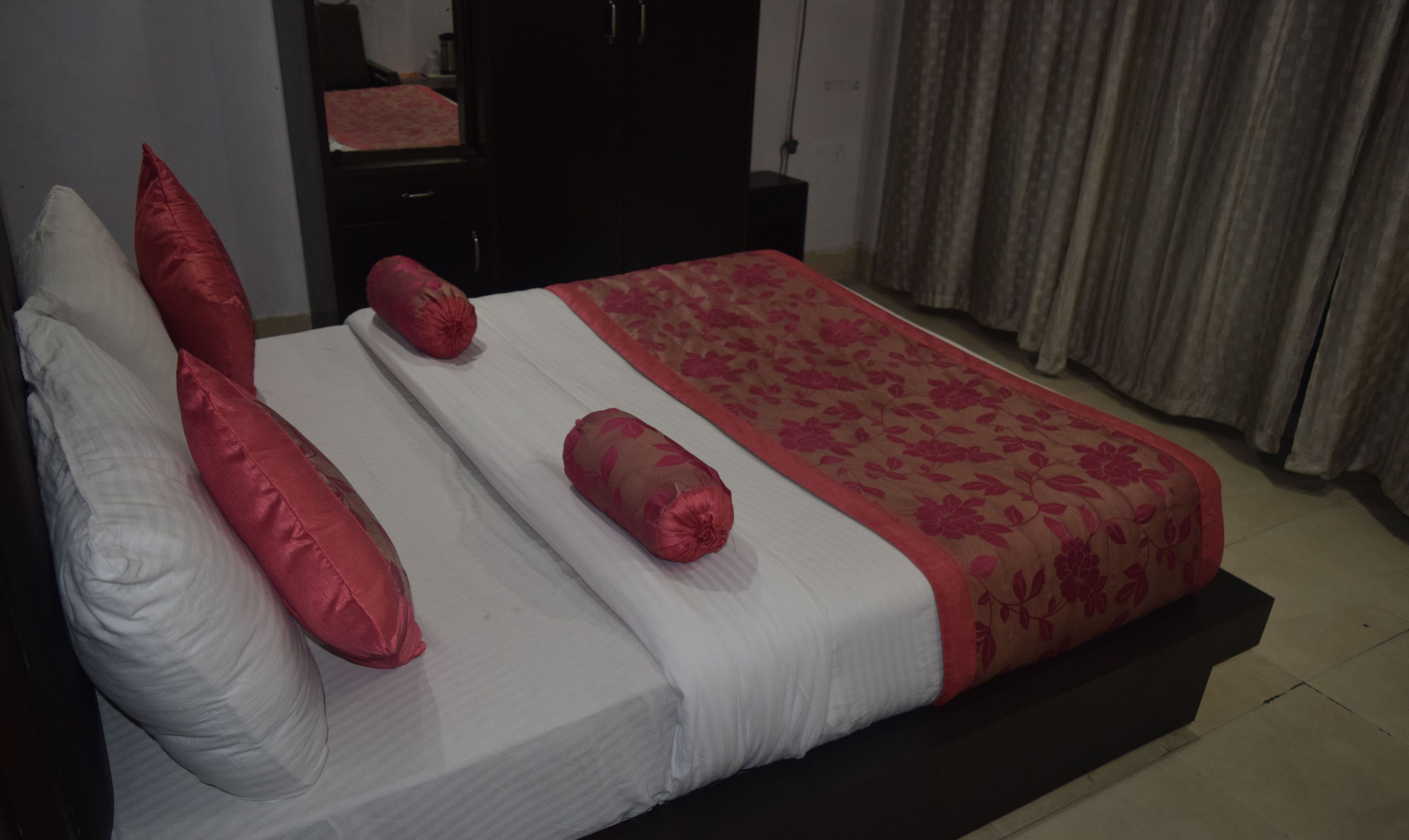 Una cama con ropa de cama blanca y roja, un cabecero oscuro y una colcha con estampado floral.