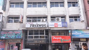 Um hotel chamado TRISHUL, com vários andares, janelas grandes e uma placa chamativa.