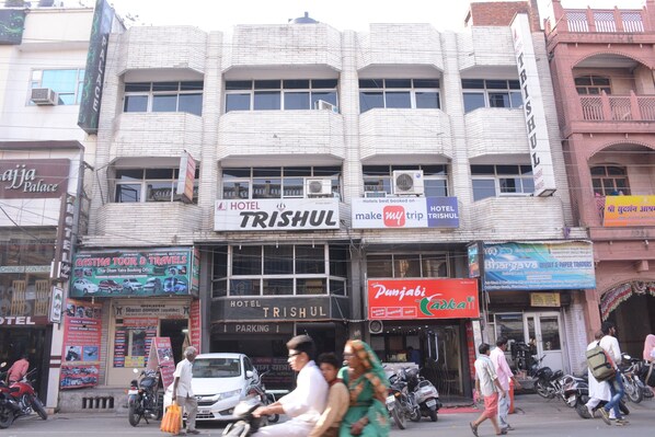 Un hotel llamado TRISHUL con un cartel que anuncia servicios de hotel y una señal de estacionamiento.