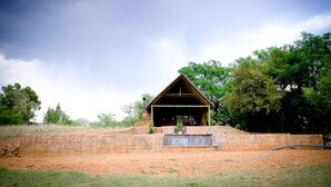 Un edificio rústico con techo inclinado, rodeado de un muro de piedra y vegetación.