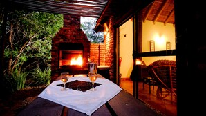 Un área de comedor al aire libre con una chimenea de ladrillo, una mesa con vasos y una vela, y una silla de mimbre.