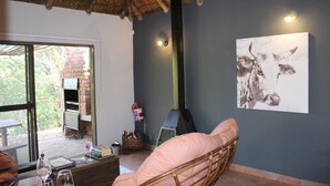 Una habitación acogedora con techo de paja, chimenea, cama y ventana grande con vista a una construcción de ladrillo.
