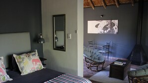 Un dormitorio con cama, espejo, televisor, chimenea y zona de estar con sillones.